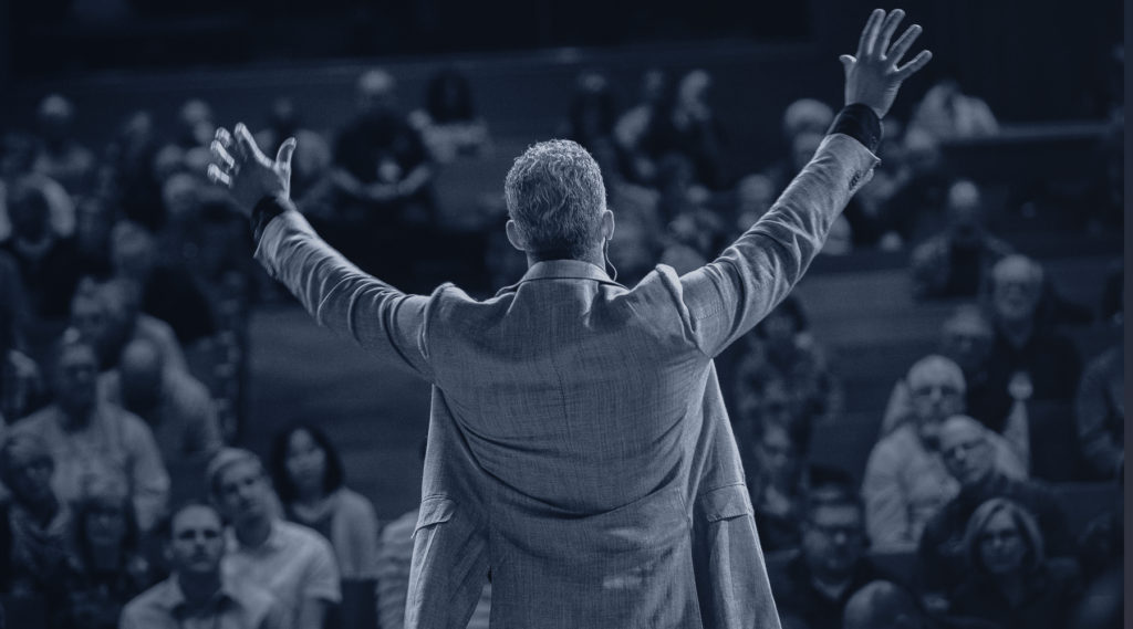 Pastor from behind with congregation in front of him, with his arms raised
