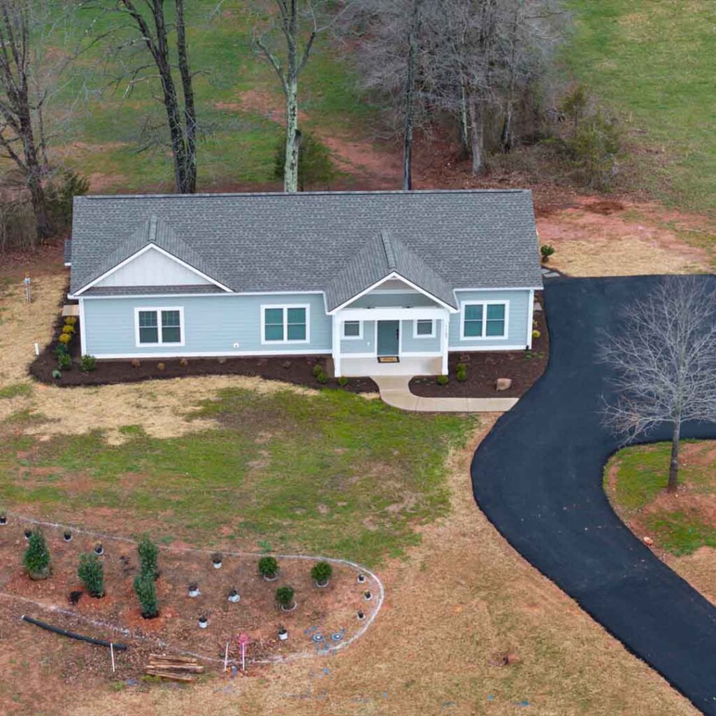 aerial view of a light blue ranch-style house with a blacktop drive way