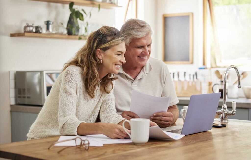 senior man and wife looking over paperwork and computer