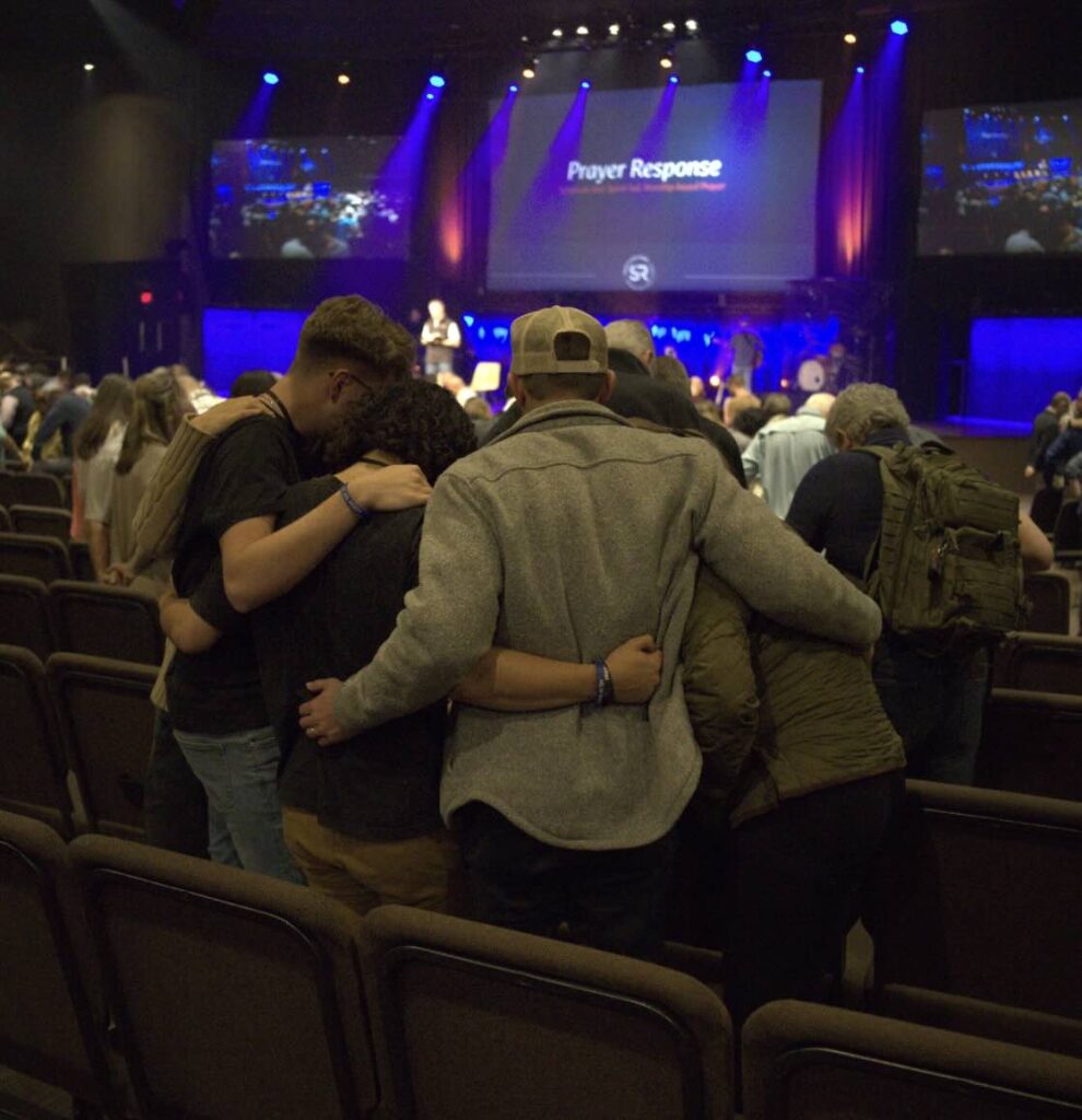 Group of young people with their arms around each other praying