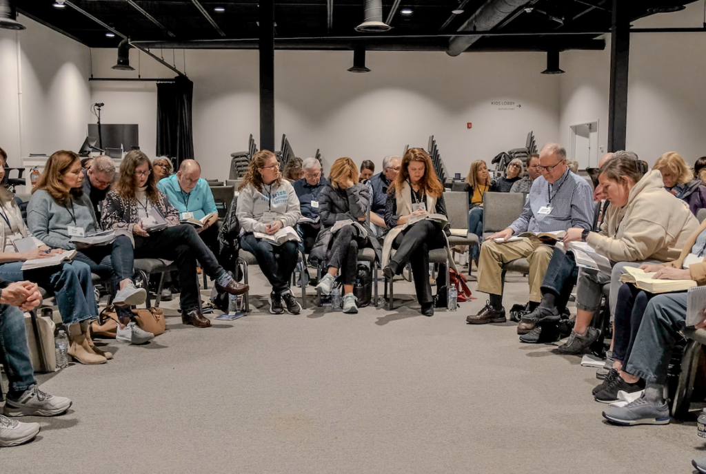 More than twenty people sitting in chairs, in concentric circles, praying with their Bibles open